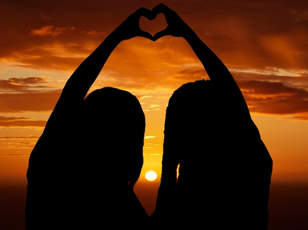 Amore libertà e cuore segno di coppia silhouette di lesbica e lgbt orgoglio a forma di mano al tramonto Le donne celebrano la relazione libera nell'amore e orgogliosa Le femmine celebrano il loro legame e stato