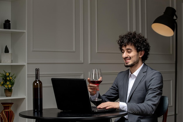 Amore virtuale bel ragazzo carino in tuta con vino su una data computer a distanza che beve vino rosso