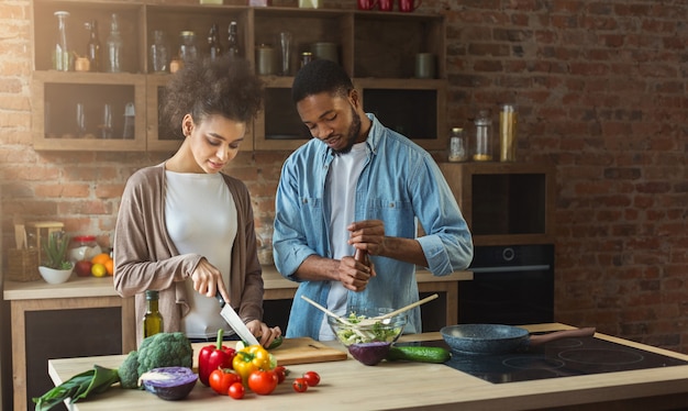 Amorevole coppia afro-americana che prepara insalata di verdure in cucina loft