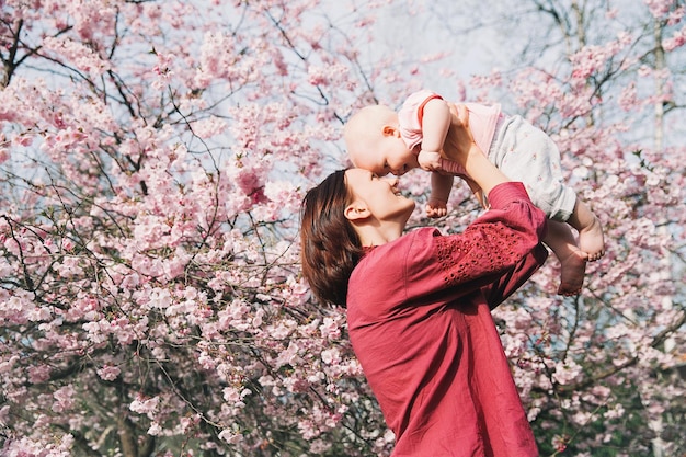 Amorevole madre e bambina su sfondo fiori rosa di melo in primavera Bella donna con figlia tra fiori da giardino all'aperto Famiglia sulla natura in Arboretum Slovenia