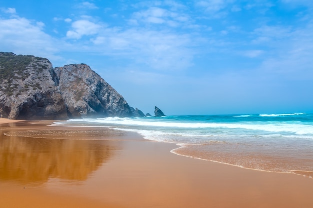 Ampia spiaggia dorata sulle rive dell'Oceano Atlantico. Costa rocciosa e surf. Cielo blu