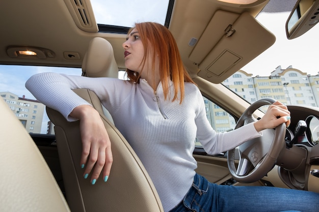 Ampio angolo di visione della giovane donna rossa alla guida di un'auto guardando indietro.