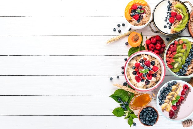 Ampio assortimento di porridge con frutta e frutti di bosco Colazione su sfondo bianco in legno Vista dall'alto Spazio libero per il testo