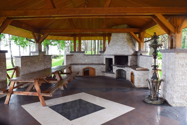 Ampio gazebo nel parco con tetto in legno e pavimento in mosaico di pietra. All'interno c'è un tavolo in legno