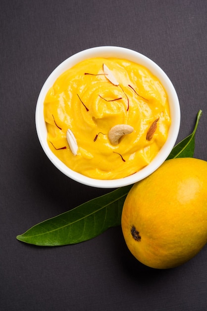 Amrakhand è uno Yogurt al gusto di Alphonso o Shrikhand, popolare dolce indiano servito con frutta secca e zafferano con frutta intera di mango, su sfondo colorato. messa a fuoco selettiva