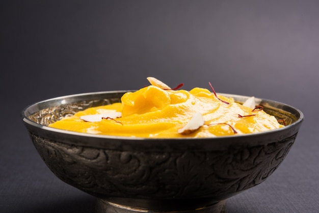 Amrakhand è uno Yogurt al gusto di Alphonso o Shrikhand, popolare dolce indiano servito con frutta secca e zafferano con frutta intera di mango, su sfondo colorato. messa a fuoco selettiva