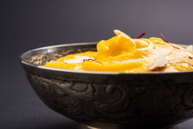 Amrakhand è uno Yogurt al gusto di Alphonso o Shrikhand, popolare dolce indiano servito con frutta secca e zafferano con frutta intera di mango, su sfondo colorato. messa a fuoco selettiva