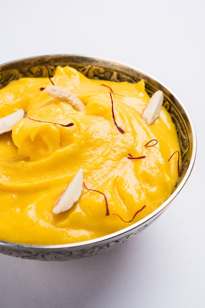 Amrakhand è uno Yogurt al gusto di Alphonso o Shrikhand, popolare dolce indiano servito con frutta secca e zafferano con frutta intera di mango, su sfondo colorato. messa a fuoco selettiva