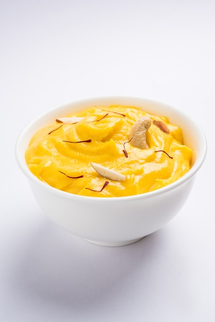 Amrakhand è uno Yogurt al gusto di Alphonso o Shrikhand, popolare dolce indiano servito con frutta secca e zafferano con frutta intera di mango, su sfondo colorato. messa a fuoco selettiva