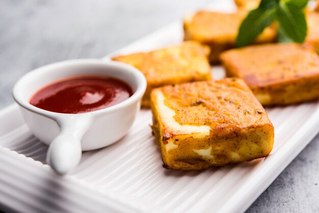 Amritsari Paneer Tikka made using cottage cheese cubes dipped in a batter made with besan, chat masala and spices and shallow fried in pan, served with ketchup