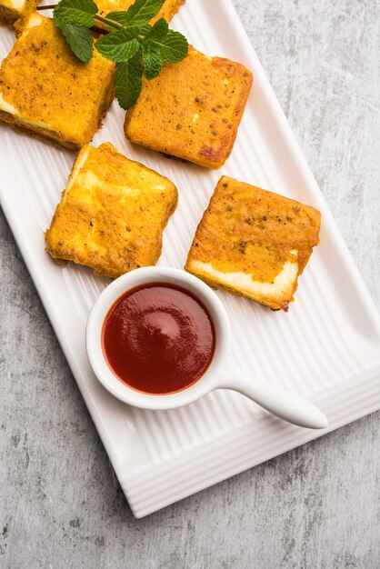 Amritsari Paneer Tikka made using cottage cheese cubes dipped in a batter made with besan, chat masala and spices and shallow fried in pan, served with ketchup