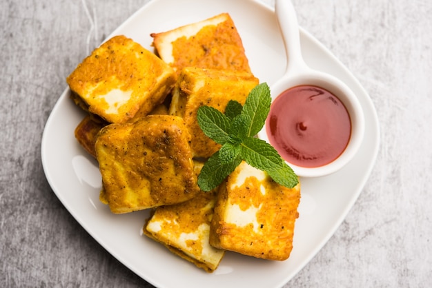 Amritsari Paneer Tikka made using cottage cheese cubes dipped in a batter made with besan, chat masala and spices and shallow fried in pan, served with ketchup