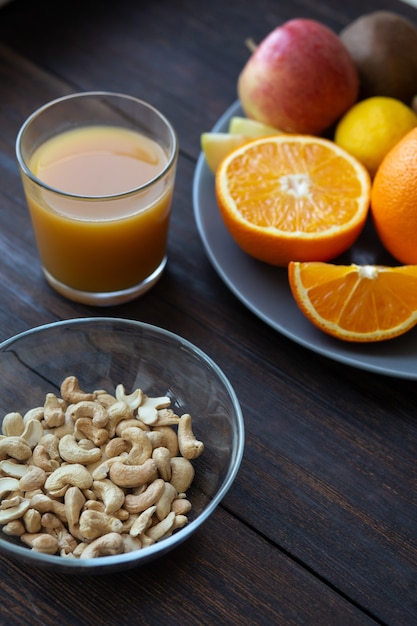 Anacardi e succo accanto ad altri frutti su un tavolo di legno nero