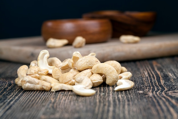 Anacardi secchi su un vecchio tavolo di legno e in una ciotola di legno, un mucchio di anacardi sul tavolo e in un piatto di legno mentre si mangia