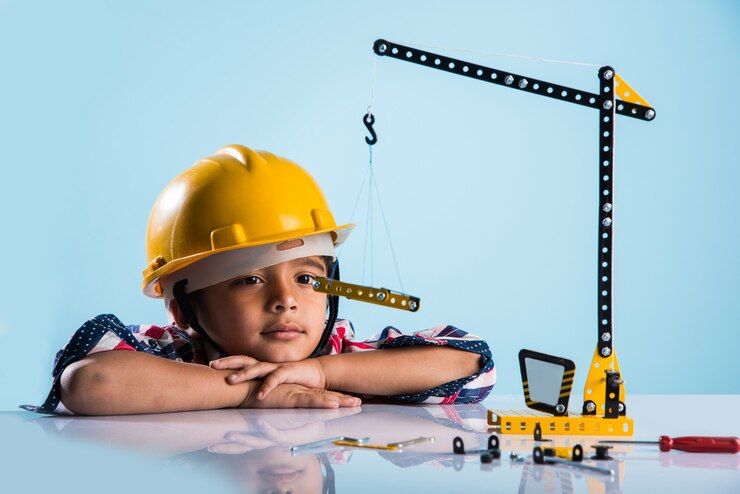 Photo anak laki-laki india kecil yang lucu bermain dengan derek mainan mengenakan topi konstruksi kuning atau helm proyek, konsep masa kanak-kanak dan pendidikan, terisolasi di atas papan tulis hijau