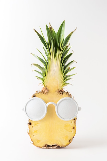 Ananas a fette con occhiali da sole bianchi su sfondo bianco.