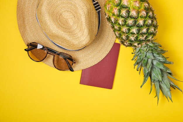 Ananas, cappello, occhiali da sole e passaporto internazionale su sfondo giallo tropici vacanza concetto copia spazio