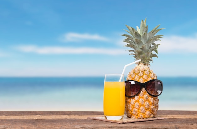 Ananas con succo sul tavolo da spiaggia e il cielo blu per il concetto di estate