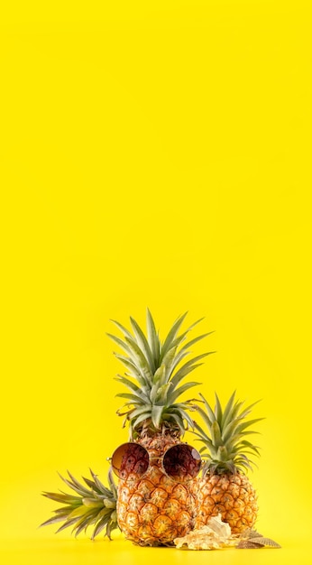 Ananas creativo che osserva in su con gli occhiali da sole e il guscio isolato su priorità bassa gialla, fine dello spazio della copia su