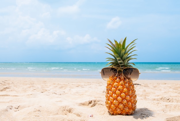 Ananas di hipster con occhiali da sole sulla spiaggia tropicale.