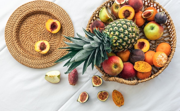 Ananas e altri frutti esotici in un cesto di vimini su uno sfondo bianco