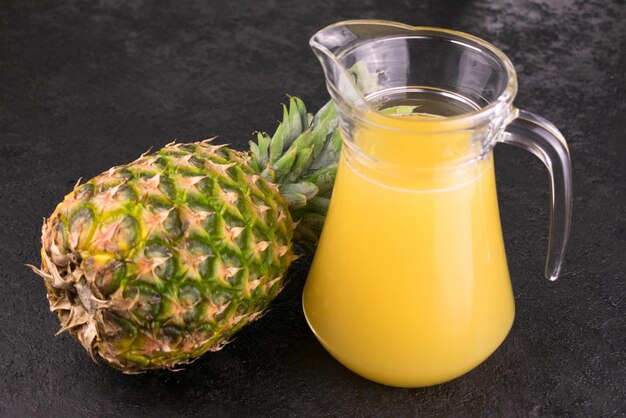 Ananas e brocca con succo di ananas su sfondo nero