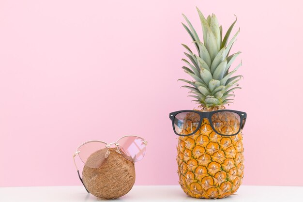 Ananas e cocco con occhiali da sole che riposano e bevono un cocktail sulla spiaggia Vacanze estive