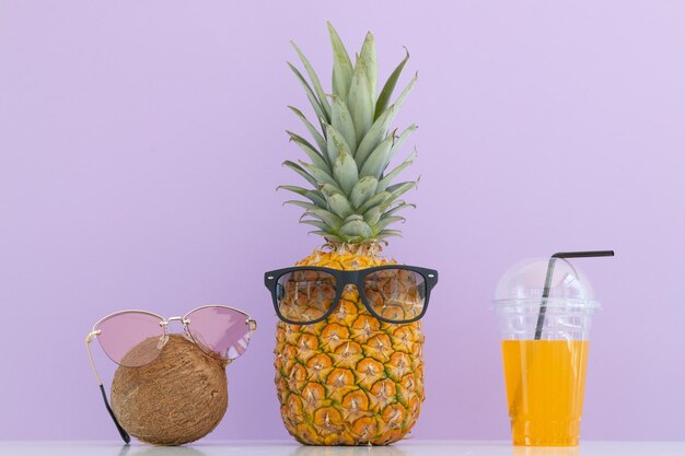 Ananas e cocco incisi con occhiali da sole vicino a un bicchiere di succo e una cannuccia da cocktail