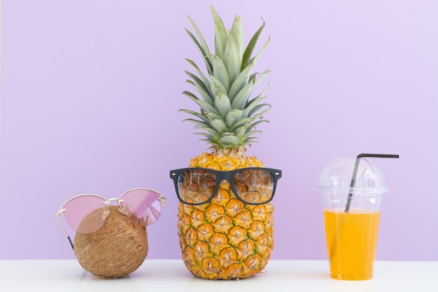 Ananas e cocco incisi con occhiali da sole vicino a un bicchiere di succo e una cannuccia da cocktail