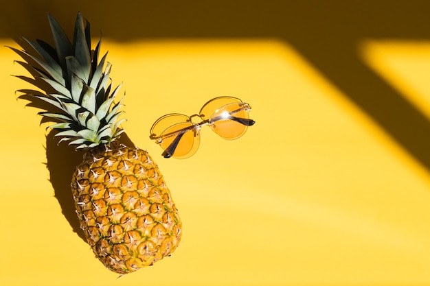 Ananas e noci di cocco hipster con occhiali da sole su sfondo giallo