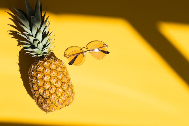 Ananas e noci di cocco hipster con occhiali da sole su sfondo giallo