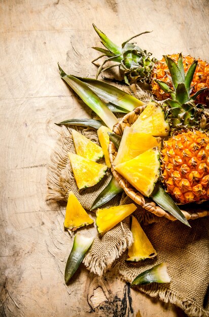 Ananas fresco, intero e affettato in un cestino sul vecchio tessuto sulla tavola di legno. Vista dall'alto