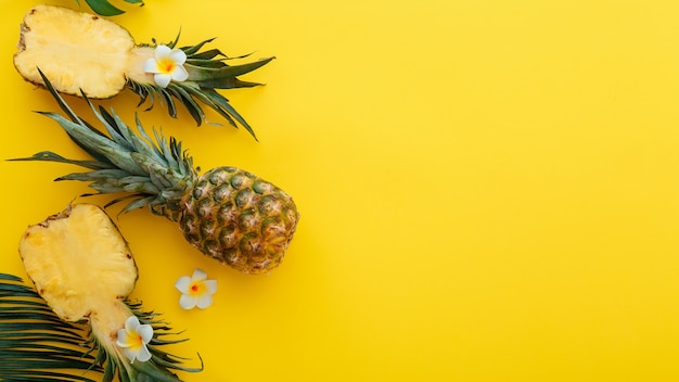 Ananas intera estate tropicale ananas frutti e metà di ananas a fette con fiori di plumeria tropicale composizione piatta laica su sfondo estivo di colore giallo. Banner web lungo con spazio di copia.