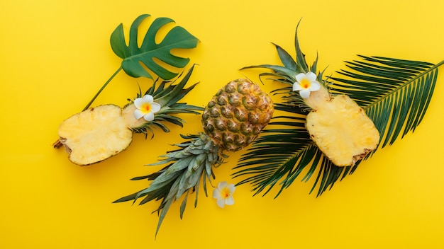 Ananas intera estate tropicale ananas frutti e metà di ananas a fette con fiori di plumeria tropicale composizione piatta laica su sfondo estivo di colore giallo. Banner web lungo.