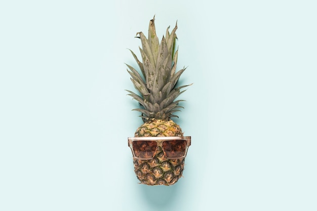 Ananas intero maturo in occhiali da sole su sfondo blu.