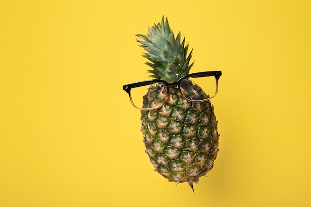 Ananas levitante con gli occhiali su uno sfondo giallo con spazio di copia