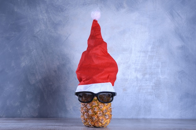 Ananas maturo, ananas con occhiali da sole nel cappello di Babbo Natale. Concetto di frutta di Capodanno