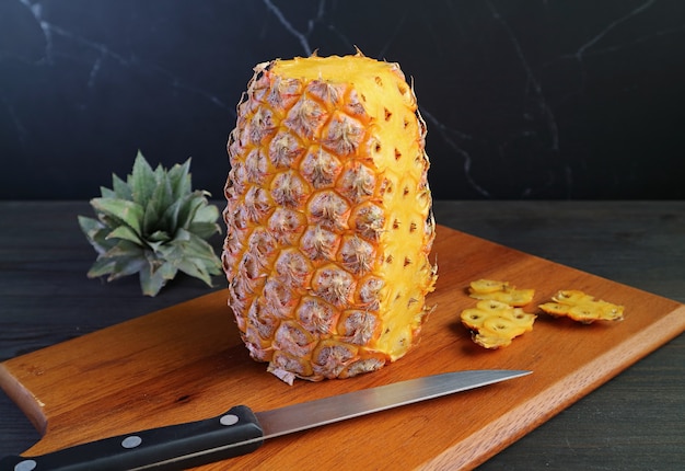 Ananas maturo fresco che viene sbucciato su un tagliere di legno