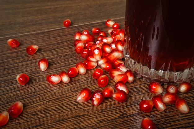 Ancora in vita un bicchiere di succo tra i chicchi di melograno sparsi sulla superficie di legno del tavolo