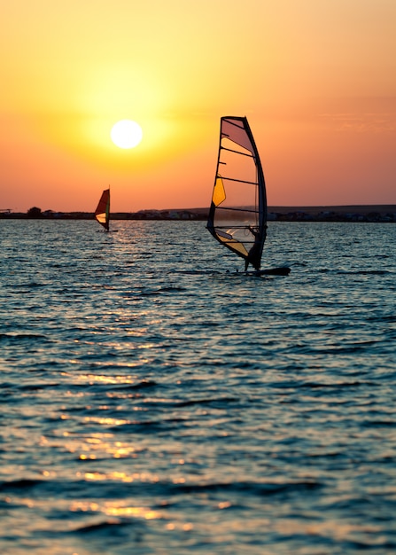 Ancora la superficie del mare, l'uomo che pratica il wind surf e il tramonto dorato nel cielo