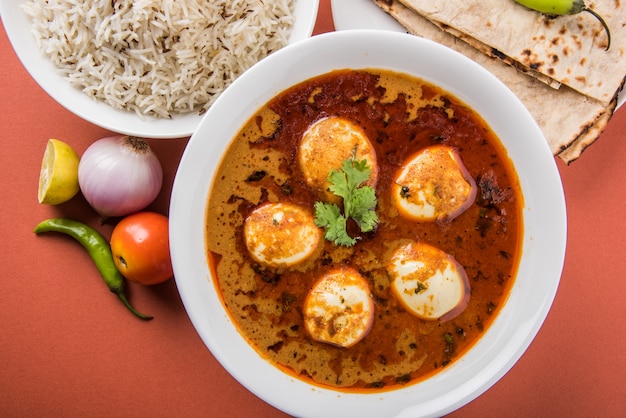 Anda Curry o sugo di masala di uova, cibo piccante indiano o ricetta, servito con riso Jeera, roti o naan, fuoco selettivo. Sopra il piano del tavolo colorato o in legno