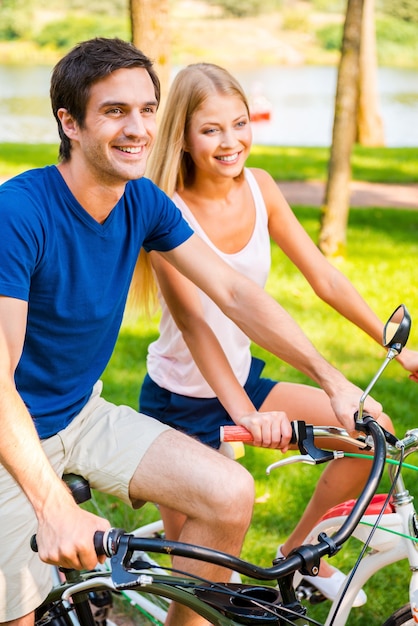 Andare in bicicletta è divertente! Bella giovane coppia sorridente in sella alle loro biciclette nel parco insieme