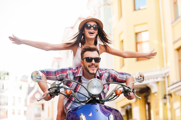 Andare in scooter insieme. Bella giovane coppia in sella a uno scooter insieme mentre una donna felice tiene le braccia tese e sorride