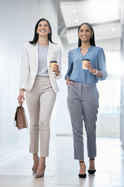 Andiamo a correre questo giorno Inquadratura di due donne d'affari che trasportano caffè mentre camminano in un ufficio