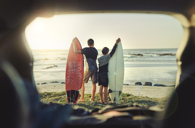 Andiamo a prendere alcune onde fratellino Inquadratura posteriore di due fratelli che tengono le loro tavole da surf mentre sono in piedi sulla spiaggia