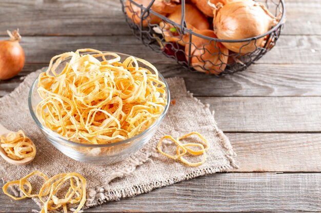 Anelli di cipolla essiccati in una ciotola di vetro su un tavolo di legno. Spezie e ingredienti alimentari. Copia spazio