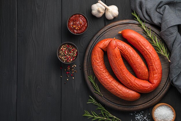 Anelli di salsiccia affumicata di Cracovia con rosmarino e salsa su un tagliere su fondo di legno nero. Vista dall'alto, copia dello spazio.