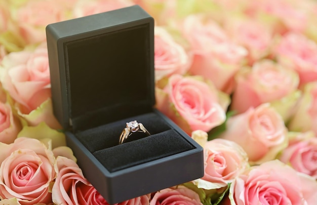 Anello di fidanzamento in oro con diamante in una custodia nera tra una grande quantità di rose in un grande bouquet da vicino