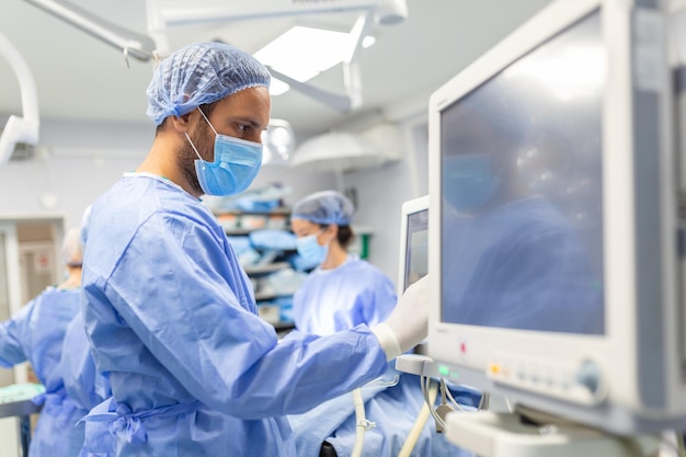 Anestesista che lavora in sala operatoria indossando dispositivi di protezione che controllano i monitor durante la sedazione del paziente prima della procedura chirurgica in ospedale