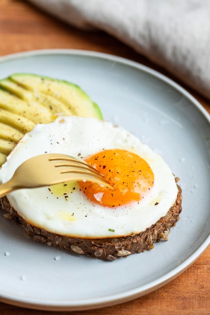 Angolo alto dell'uovo fritto della prima colazione sulla zolla con l'avocado e la forcella